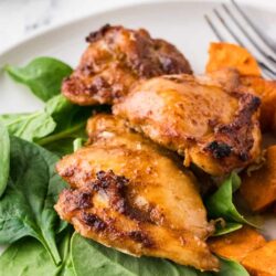 Juicy roasted chicken thighs with fresh spinach and sweet roasted carrots on a white plate. Perfect for easy weeknight dinners.