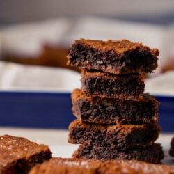 Rich, gooey brownies stacked on a white and blue plate, with some broken edges in the foreground.