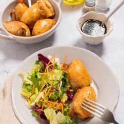 Baked Bree roasted chicken drumsticks with fresh garden salad on a white plate.