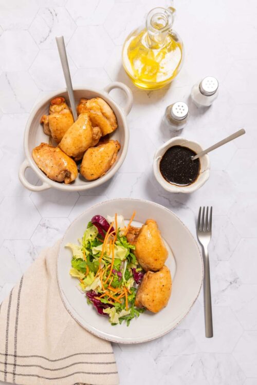 Golden baked chicken drumsticks on a serving plate with fresh salad, seen from a top view.