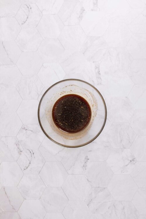 Soy sauce in a glass bowl on a white marble hex tile surface.