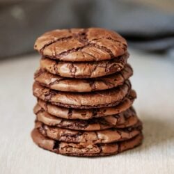 Homemade chocolate chip cookies stacked on a light surface.