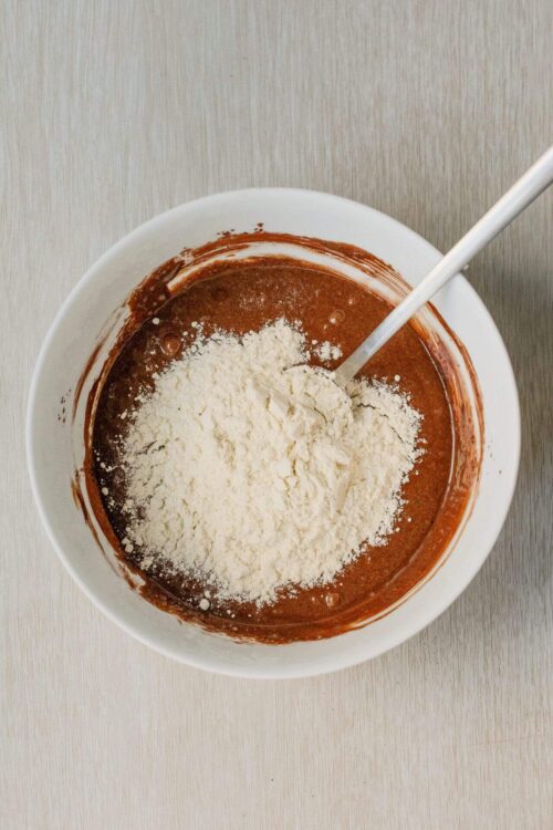 Flour added to chocolate cake batter in a mixing bowl for baking Recipe.