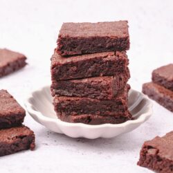 Gooey chocolate brownies on a white plate with additional brownies surrounding it.