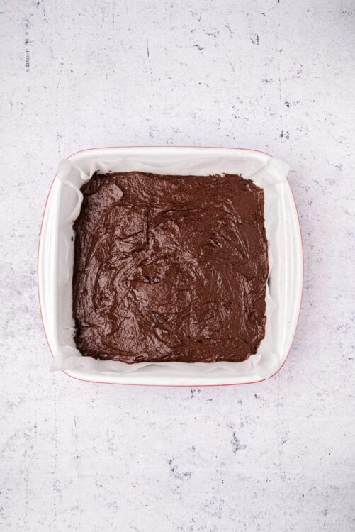 Rich chocolate brownie batter in a square baking dish with parchment paper.
