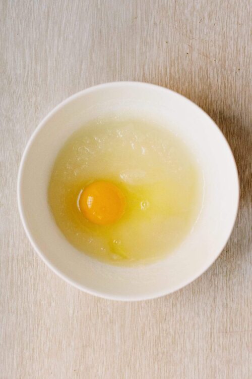 Fresh cracked egg in a white bowl for baking recipes.