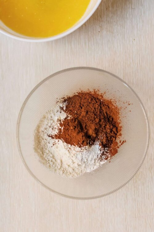 Ground cinnamon, cocoa powder, and flour in a glass bowl for baking recipes.