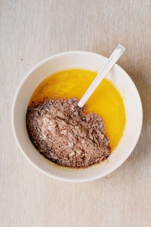 Flour, eggs, and sugar for baking in a white bowl on a wooden surface.