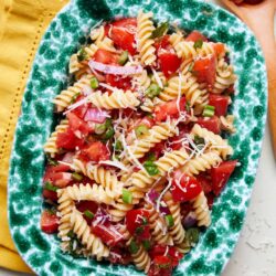 Fresh pasta salad with tomatoes, green onions, and shredded cheese on a decorative green plate.
