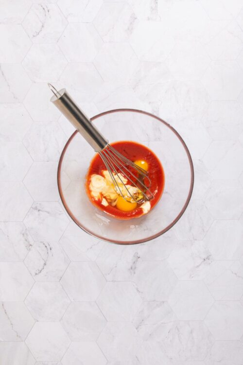 Cream mixture with eggs and tomato sauce in glass bowl for baking.