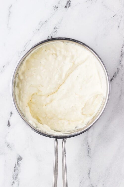 Creamy mashed potatoes in a stainless steel saucepan on white marble surface.