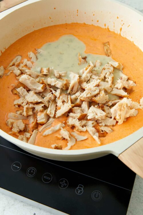 Creamy tomato soup with shredded chicken and drizzled cream, cooked on a modern electric stove.