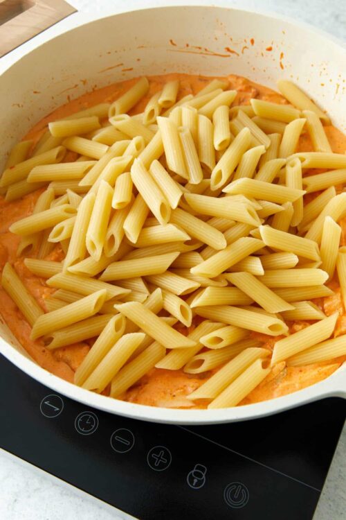 Pasta being added to a creamy tomato sauce in a white skillet.
