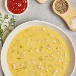 Creamy chicken and celery soup with fresh vegetables and seasonings on a white plate.