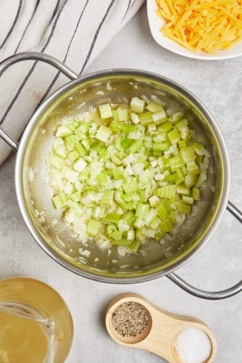 Chopped celery sautéing in a stainless steel pan for cooking recipes.