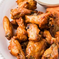 Crispy baked chicken wings served with dipping sauce and carrot sticks on a white platter.