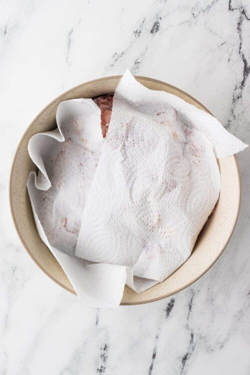 Raw chicken in a baking dish with paper towels for patting dry.