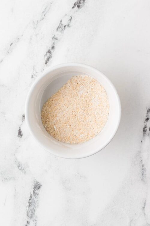 Finely ground bread crumbs in a white bowl on a marble surface.