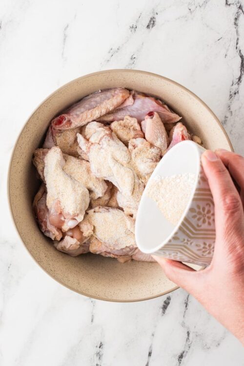 Breaded chicken pieces in a bowl ready for cooking, with a person adding flour or breading mixture, suitable for baked chicken recipes.