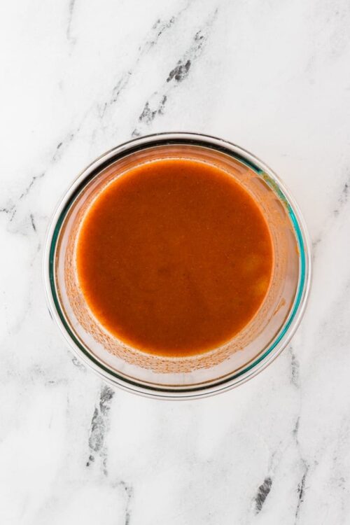 Savory tomato soup in a glass bowl on white marble surface.