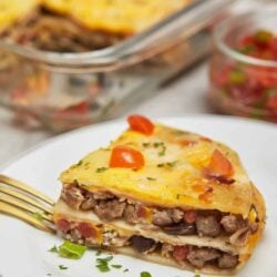 Cheesy beef taco lasagna slice on white plate with fresh herbs.