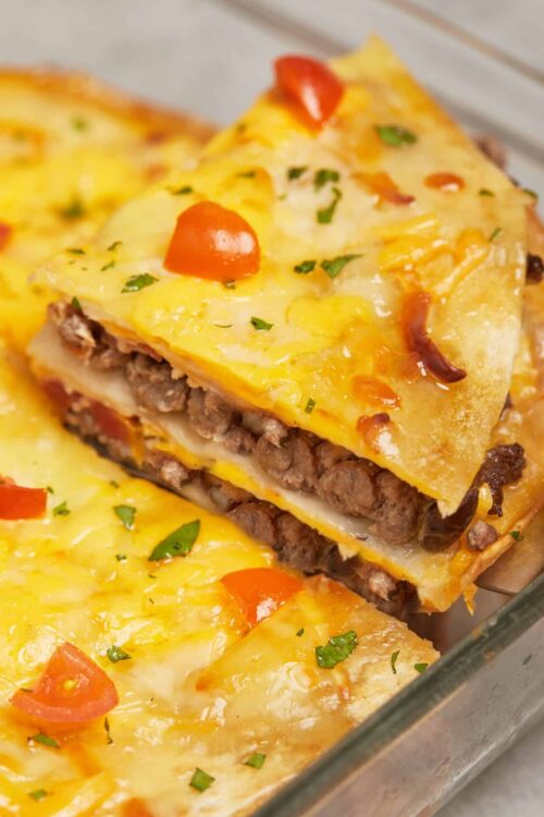 Cheesy Mexican casserole with ground beef, tomatoes, and fresh herbs in a baking dish.