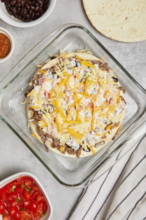 Cheesy baked casserole with ground beef, tomatoes, and shredded cheese in glass baking dish.