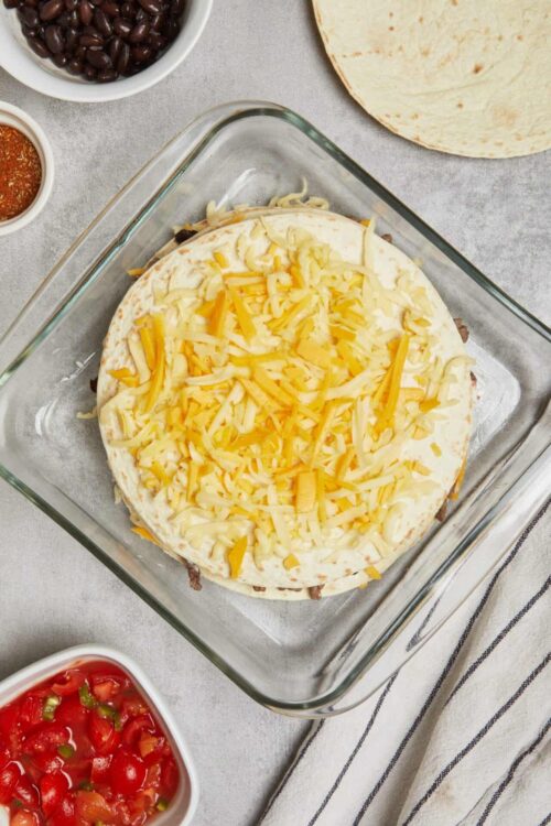 Golden shredded cheese layered on a taco casserole before baking.