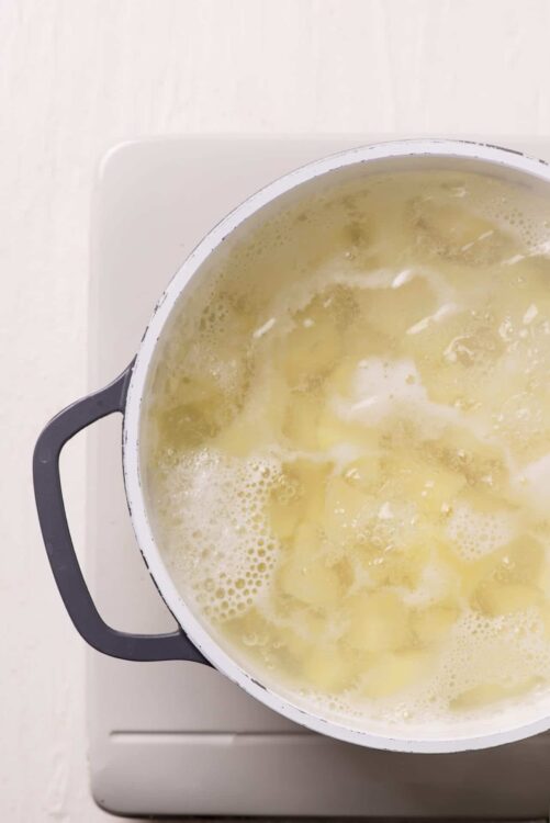 Creamy potato soup cooking in a white enamel pot on a stovetop, perfect for comfort food recipes.