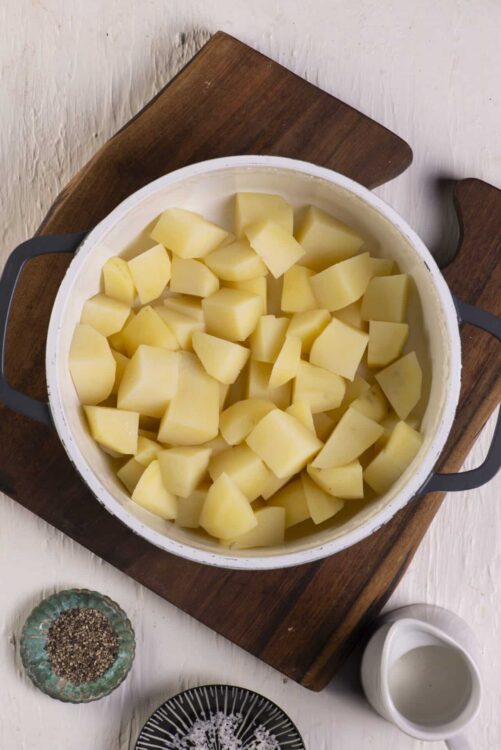 Creamy peeled potatoes for mashed potatoes, on a rustic wooden cutting board.