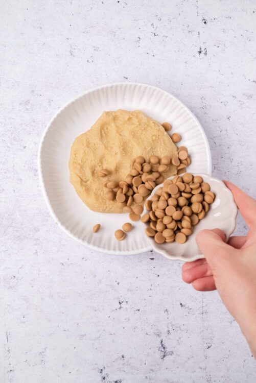 Softened cookie dough with white chocolate chips and beige chocolate chips on a white plate.