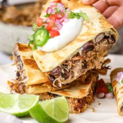 Crockpot Mexican shredded beef burritos with toppings and lime wedges.