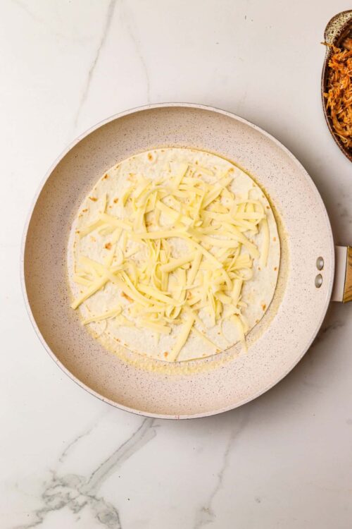 Cheese melting on a flour tortilla in a non-stick skillet, ideal for quesadillas or grilled cheese sandwiches.