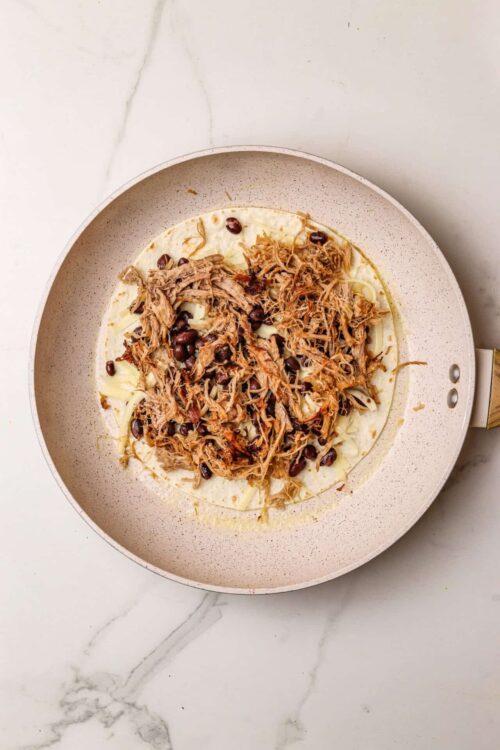 Shredded pork with black beans on a tortilla in a skillet.