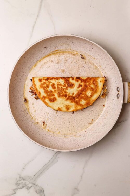 Golden brown grilled quesadilla on non-stick skillet, delicious and cheesy Mexican-inspired dish.
