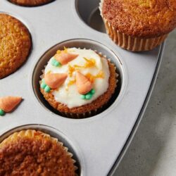 Frosted cupcakes in a metal baking tray with sprinkles and icing decorations.