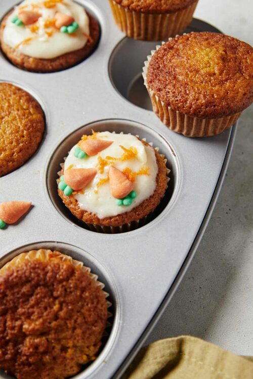 Frosted cupcakes in a metal baking tray with sprinkles and icing decorations.