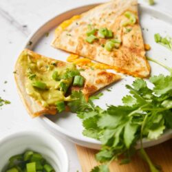 Freshly made quesadillas with melted cheese and green onions served on a white plate.
