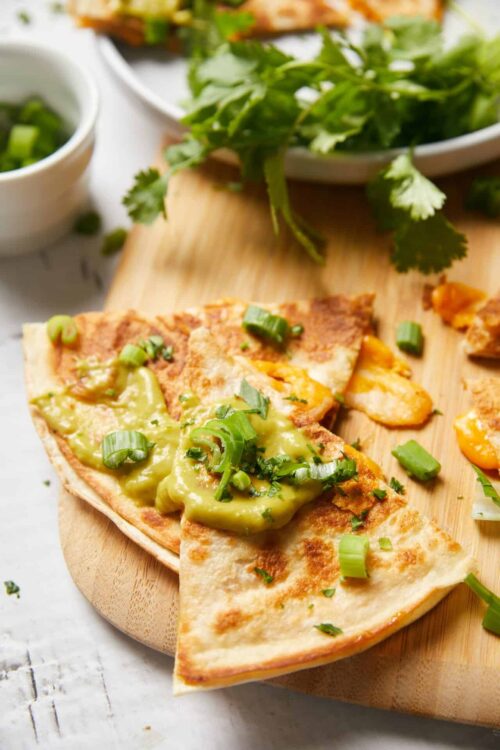 Crispy quesadilla with melted cheese and green onions on wooden serving board.