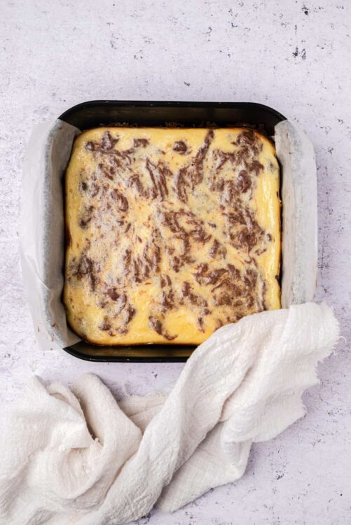 Cream cheese and cinnamon swirl cheesecake in a baking pan with parchment paper.