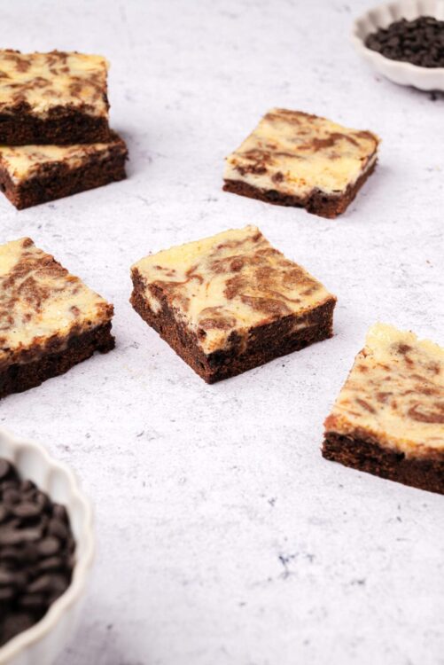 Rich marble cheesecake bars with a chocolate and vanilla swirl on a white surface.