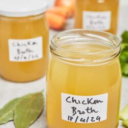 Fresh homemade chicken broth in glass jars with labels, prepared for cooking or freezing.