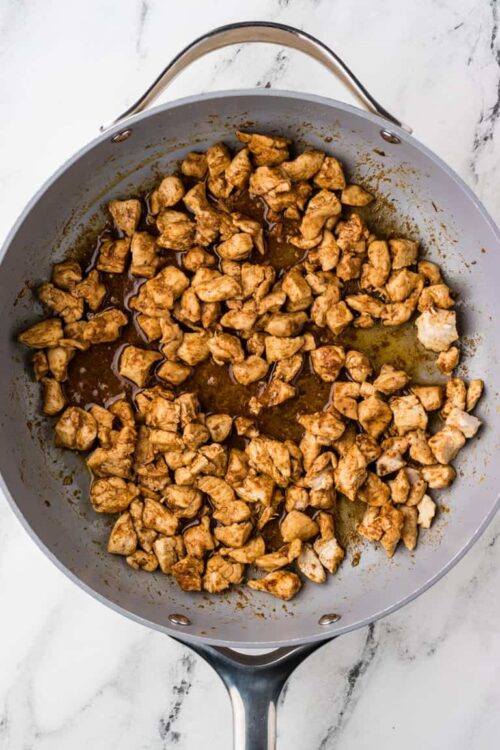 Cubed cooked chicken in a skillet with sauce, cooking step for chicken recipes.