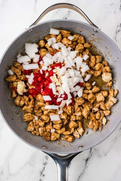 Cooked chicken with onions, garlic, and red bell pepper in a skillet for delicious recipes.