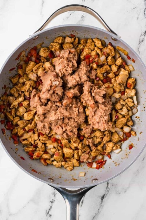 Cooked chicken and vegetable mixture in a skillet with raw ground chicken on top for a recipe.
