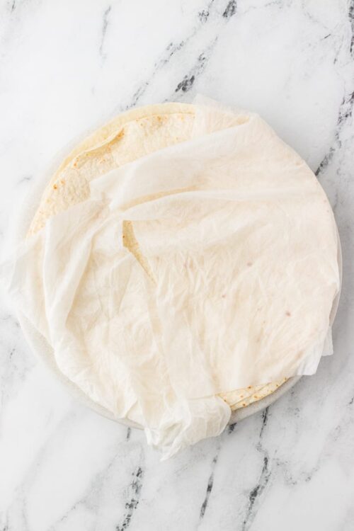 Soft flour tortillas wrapped in parchment paper on a marble surface.