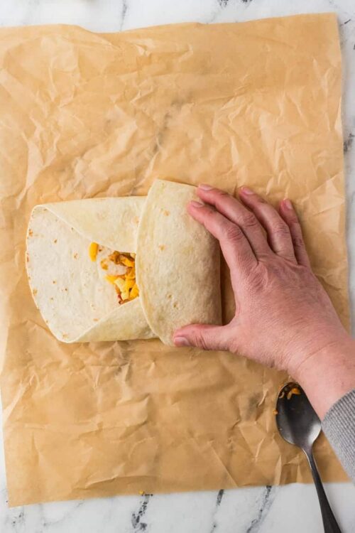 Soft flour tortilla with shredded cheese and chicken filling on brown parchment paper.