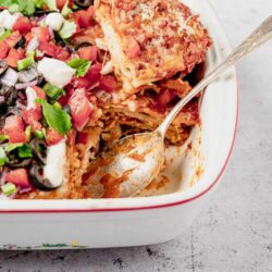 Baked ziti pasta casserole with marinara, cheese, and fresh side salad in a white baking dish.