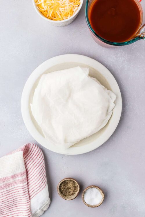 Flaky puff pastry dough on a white plate with ingredients for baking.