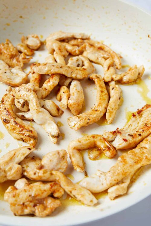 Grilled chicken strips cooking in a white skillet for healthy chicken dinner recipes.